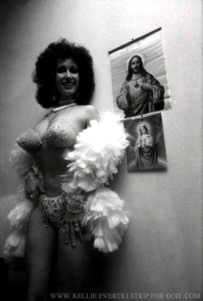 Kellie standing 10 feet tall  in ornate, sequinned brazier and white feather boa next to hanging paintings of the Blessed Virgin Mary and Jesus Christ