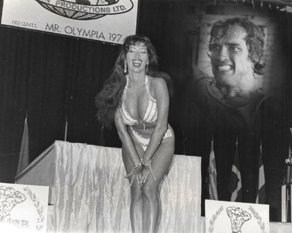 Haha. Buxom bikini Kellie gives a drop-dead winning pose on stage at the 1974 Mr. Olympia contest. Why is Arnold so pissed? Kellie won two trophies and Arnold only one! Lou Ferrigno was a fellow contestant at this bodybuilding event