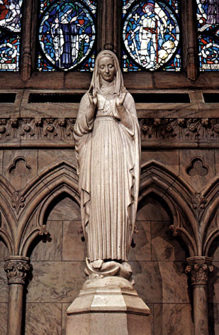Statue of the Blessed Virgin Mary of the Immaculate Heart, inside ornate, classical cathedral with allegorical stained glass depictions behind.