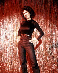 Kellie, the Stripper full clothed, on stage in black denim pants, hair done in perm and tight blask top, standing in the spotlight